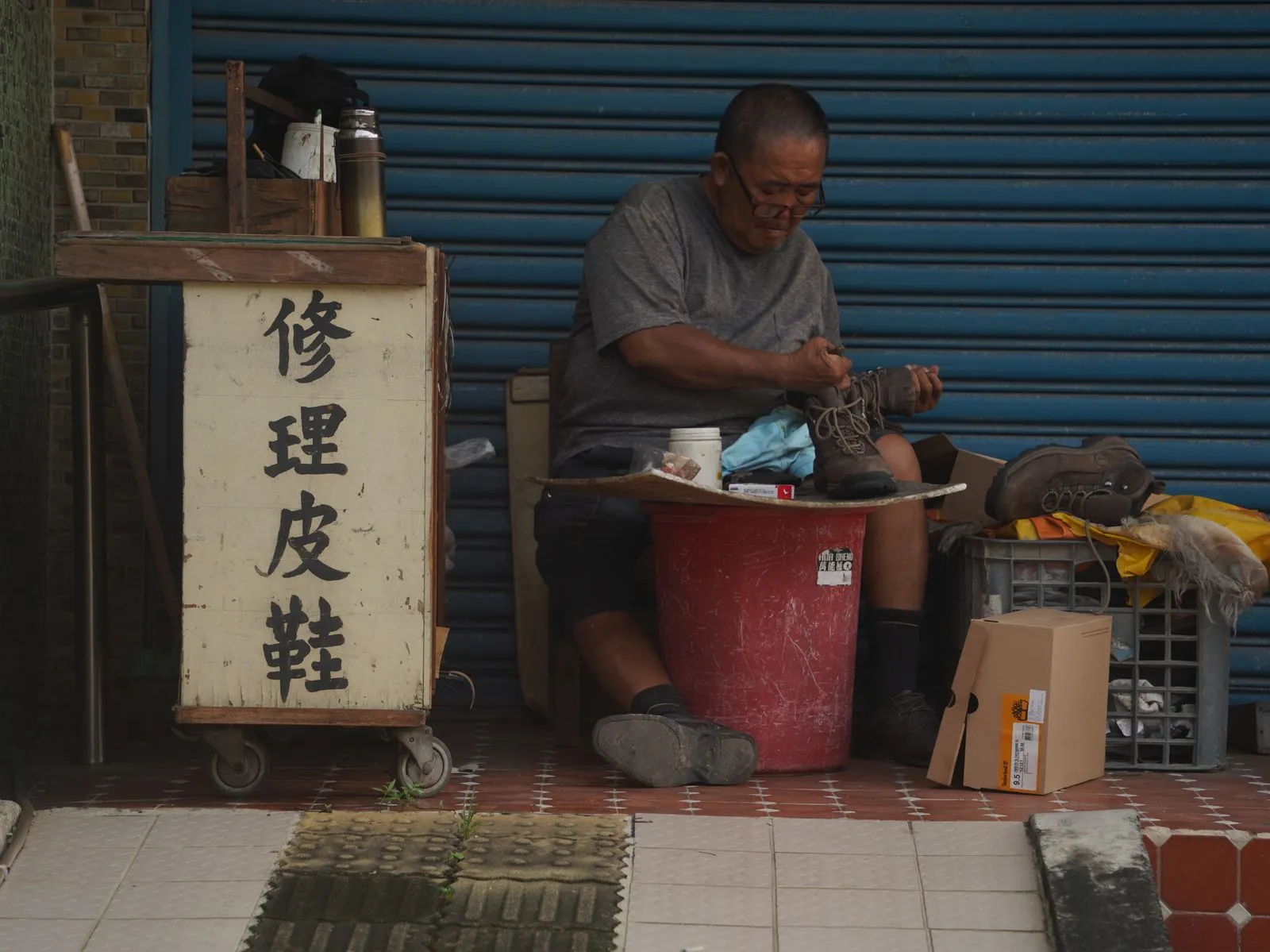 Elderly man repairing shoes on a Taiwan city sidewalk. Urban candid scene.